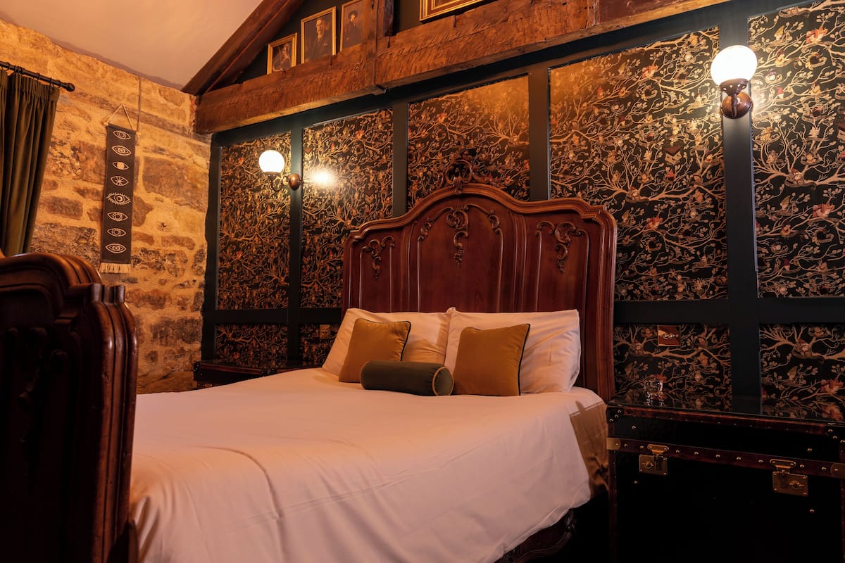 A bed with a wooden headboard, a nightstand, and a wall with a floral pattern.