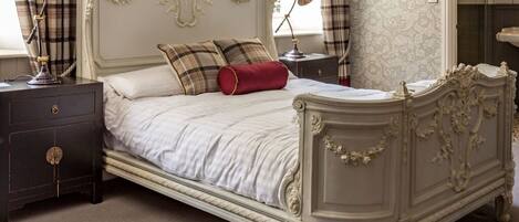 A classic bed with ornate headboard and footboard, a bedside table with a lamp, and a dark nightstand.