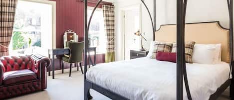 Una cama con dosel con cubrecama blanco, un sofá de cuero rojo y un escritorio con silla en una habitación con paredes rojas y un ventanal grande.