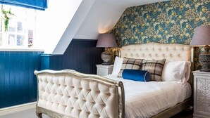 Une chambre à coucher avec un lit classique, une tête de lit décorée et un papier peint à motifs floraux.