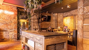 Un intérieur rustique avec un bar en bois, des murs en briques et des plantes suspendues.