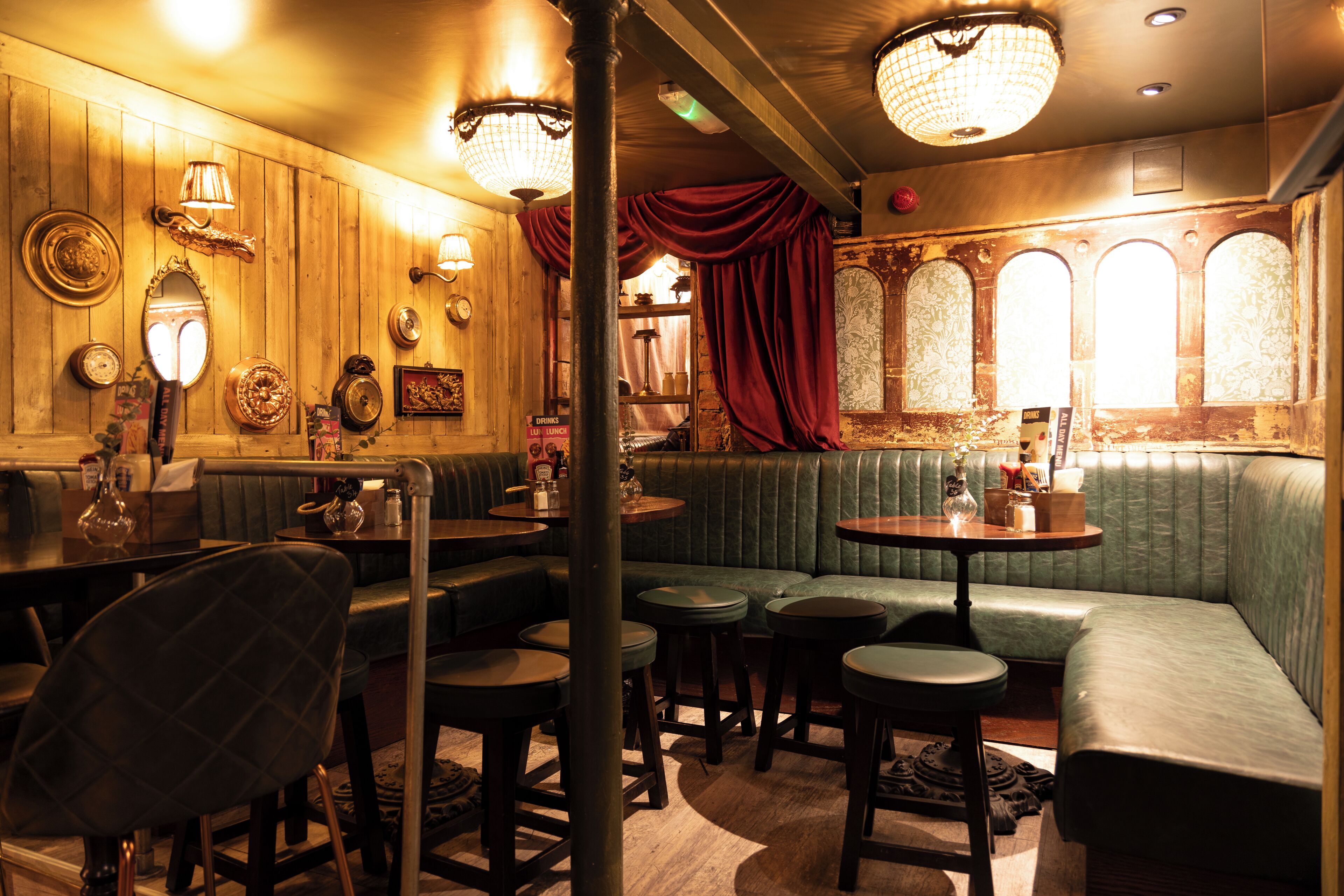 Un restaurant chaleureux avec des murs en bois, des sièges recouverts d’un tissu vert et un décor classique.