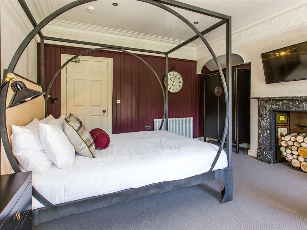 A bedroom with a four-poster bed, a clock, a fireplace, and a television mounted on the wall.