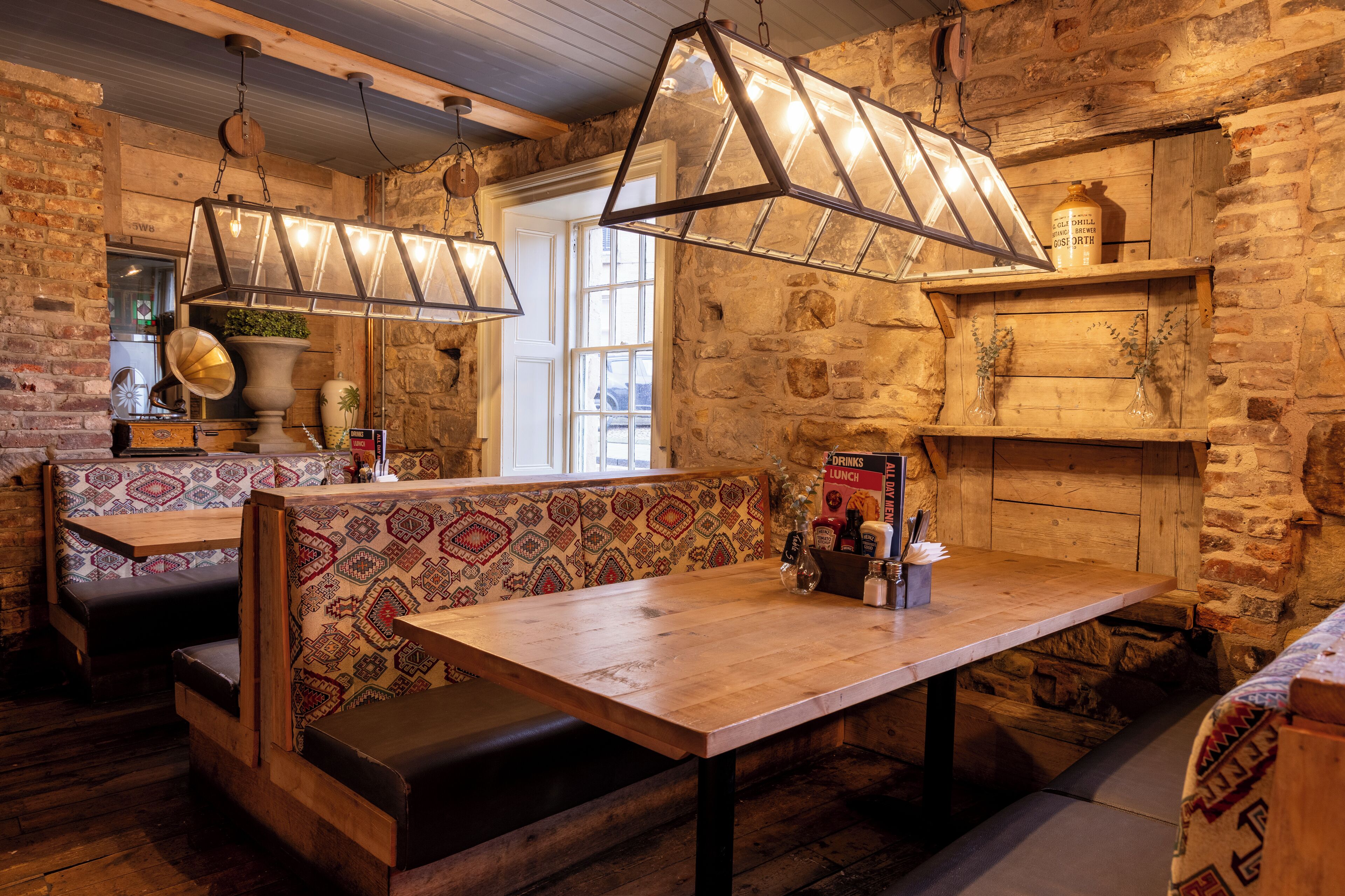 A rustic interior with stone walls, wooden benches, and a long table with a menu.