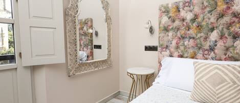 A bedroom with a bed, a mirror, a small round table, and a floral headboard.