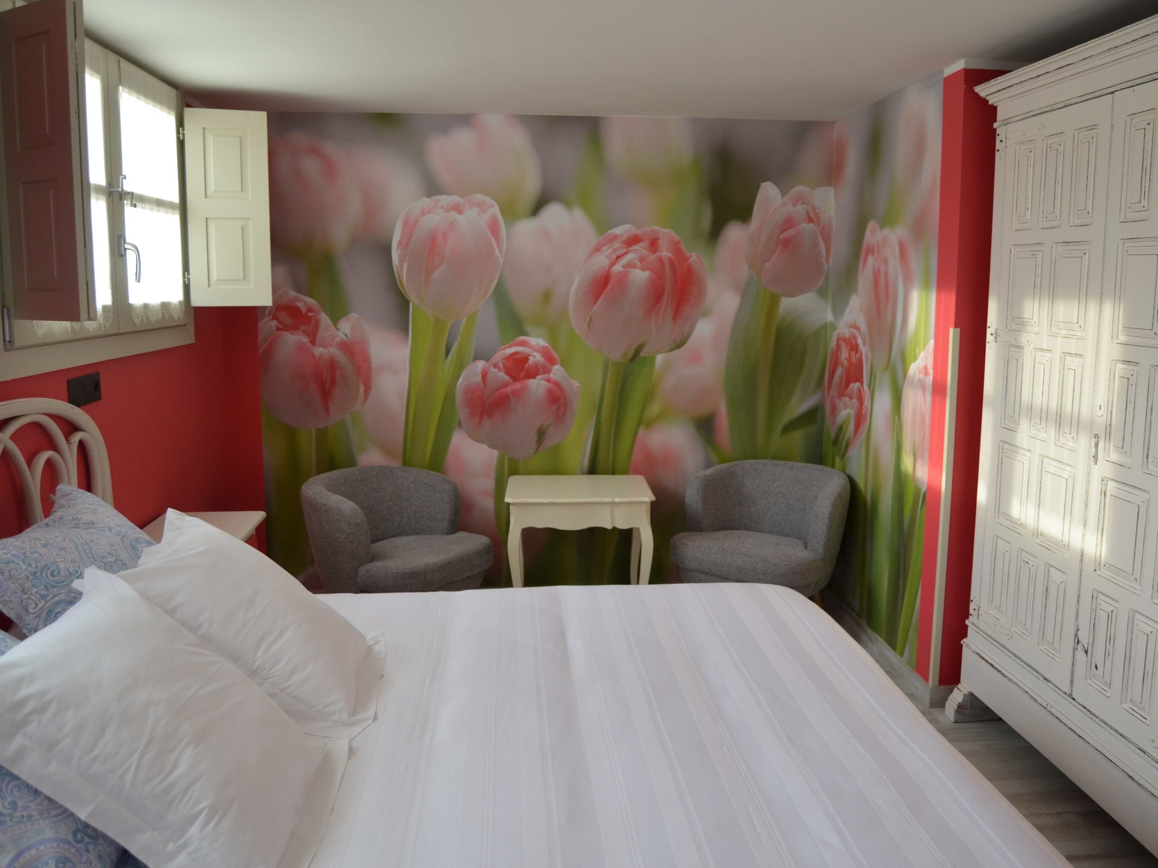 Une chambre à coucher comprenant un lit, deux fauteuils, une petite table et une fresque murale représentant des tulipes roses.