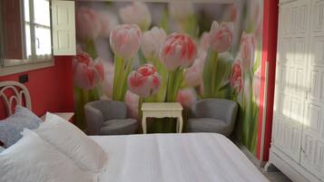 Une chambre à coucher comprenant un lit, deux fauteuils, une petite table et une fresque murale représentant des tulipes roses.