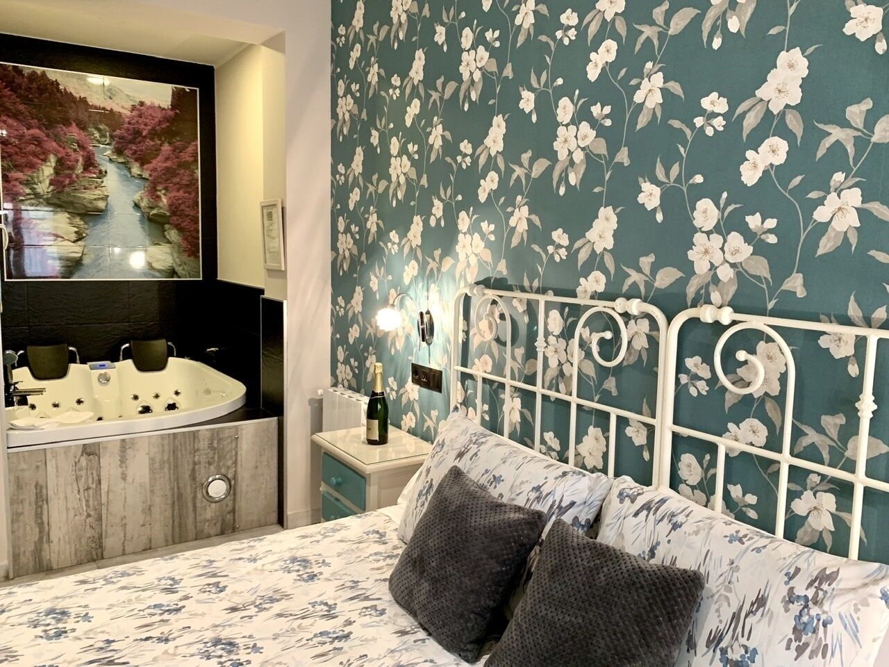 A bedroom with a bed, a nightstand, a mirror, a sink, and a floral wallpaper.