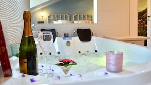 Una bañera de hidromasaje con una botella de champán, una copa de martini y una vela, rodeada de pétalos de flores.