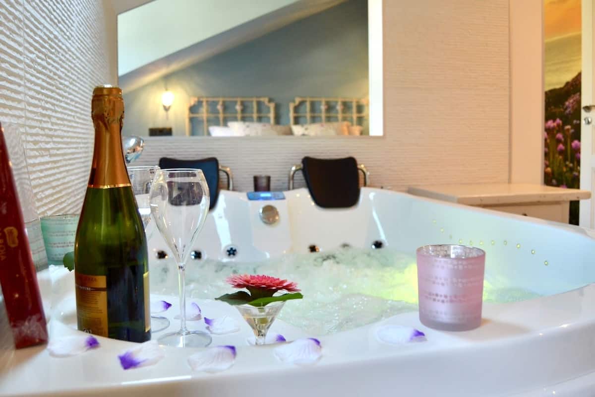 Una bañera de hidromasaje con una botella de champán, una copa de martini y una vela, rodeada de pétalos de flores.