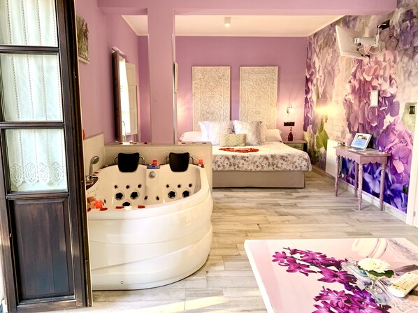 Een slaapkamer met een groot bad, een bed met een bloemenbedekking en een muur met een bloemenmuurdecoratie.