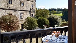 A balcony with a table set for breakfast overlooking a historic stone building and a scenic countryside view. - Akla Hotel Suites Santillana (Santillana del Mar)
