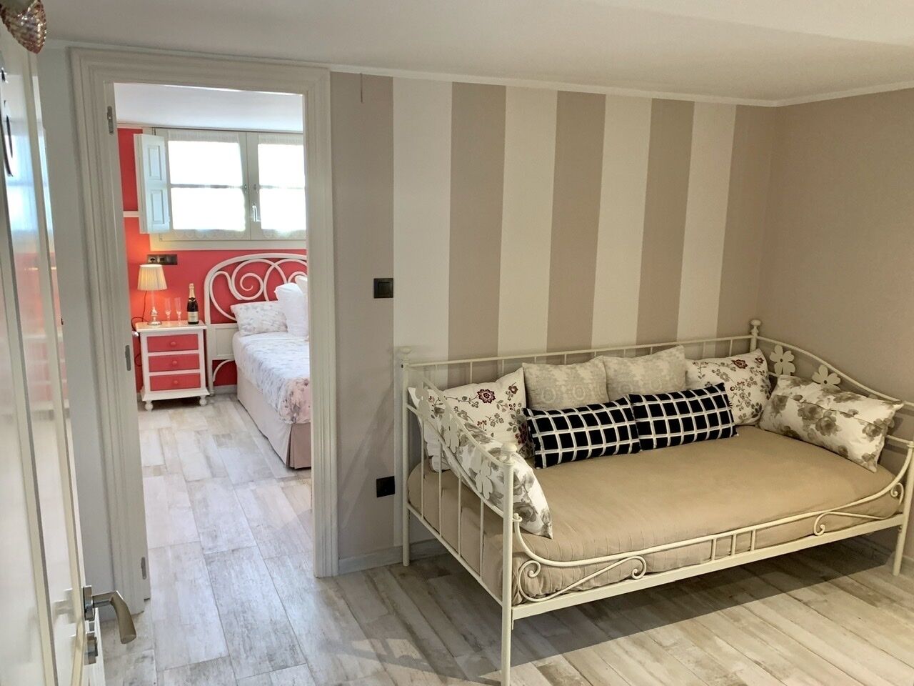 Une chambre à coucher avec un lit en métal, une table de chevet rouge et une fenêtre avec des rideaux.