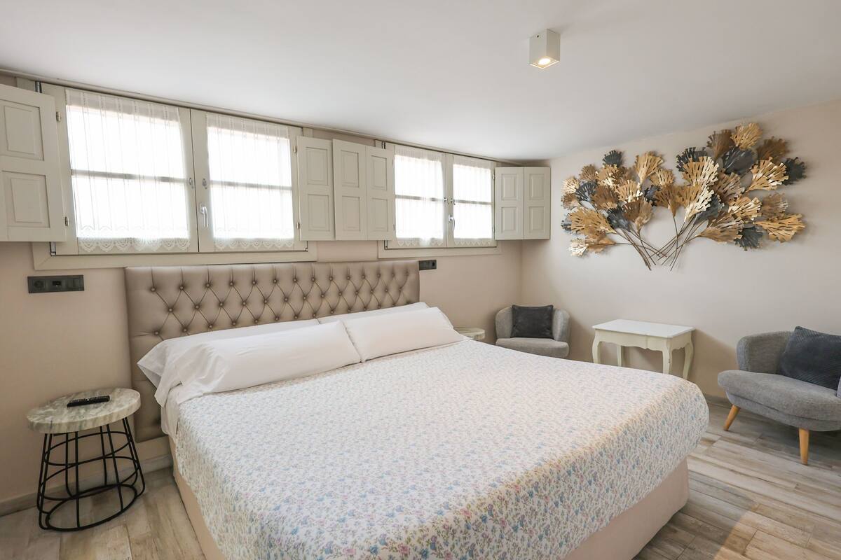 Un dormitorio con una cama grande, una mesita, una silla y un adorno en la pared.