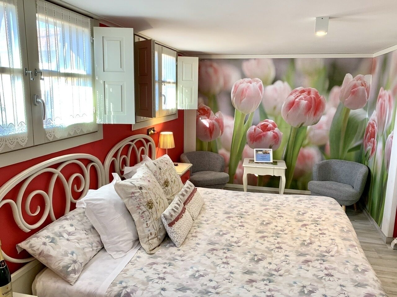 Une chambre à coucher avec un lit, des oreillers, une table de chevet, une lampe, une chaise et une fresque florale sur le mur.