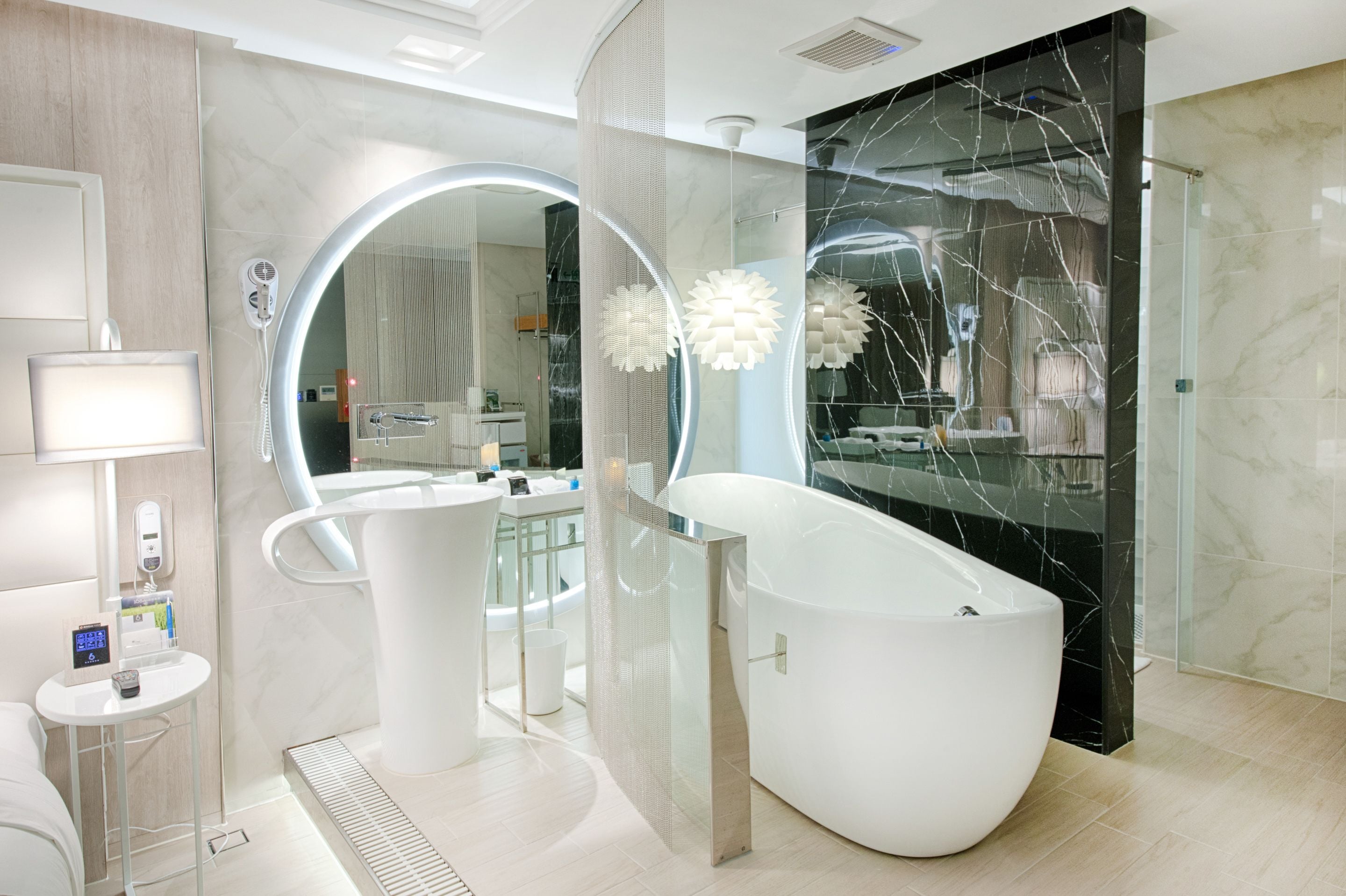 A modern bathroom with a freestanding bathtub, a round mirror with a light, and a glass partition.