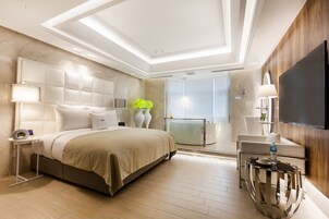Un dormitorio moderno con una cama grande, mesitas de noche, un televisor y un separador de vidrio.