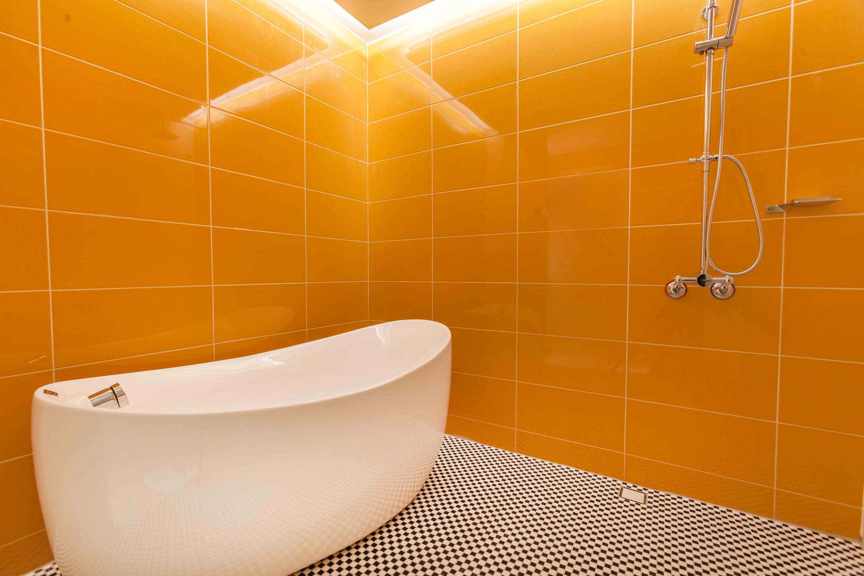 Un baño con una bañera blanca, ducha y paredes de azulejos naranja.