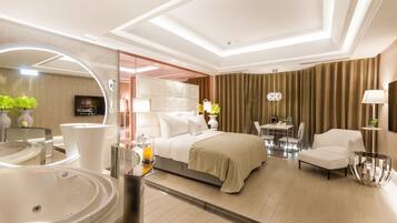 A modern hotel room with a large bed, a sitting area with a table and chairs, a separate bathroom with a large mirror and sink, and a television.