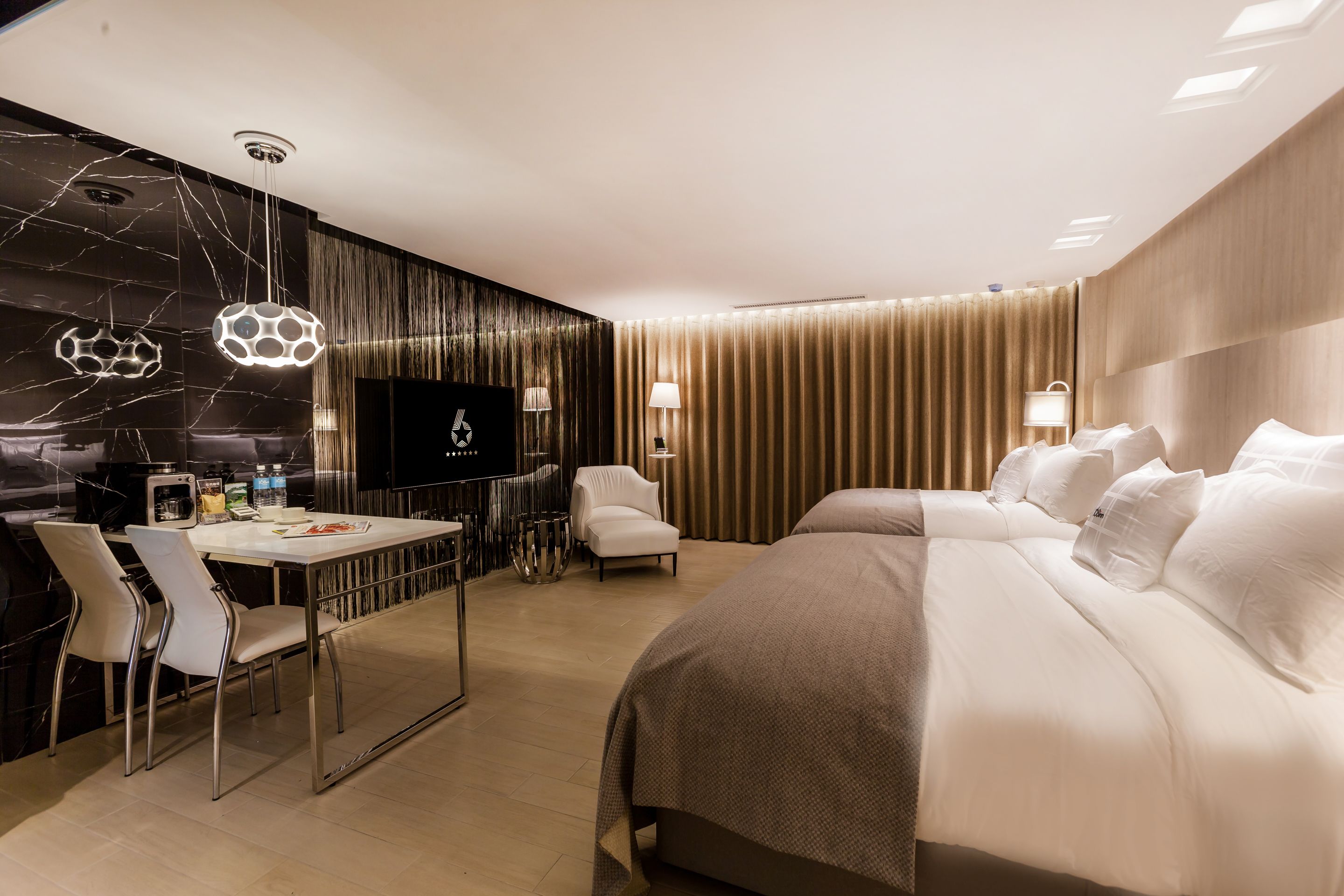 A modern hotel room with a large bed, a desk with chairs, a television, and a minibar.
