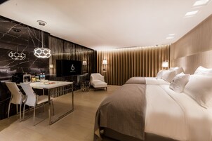 A modern hotel room with a large bed, a desk with chairs, a television, and a minibar.