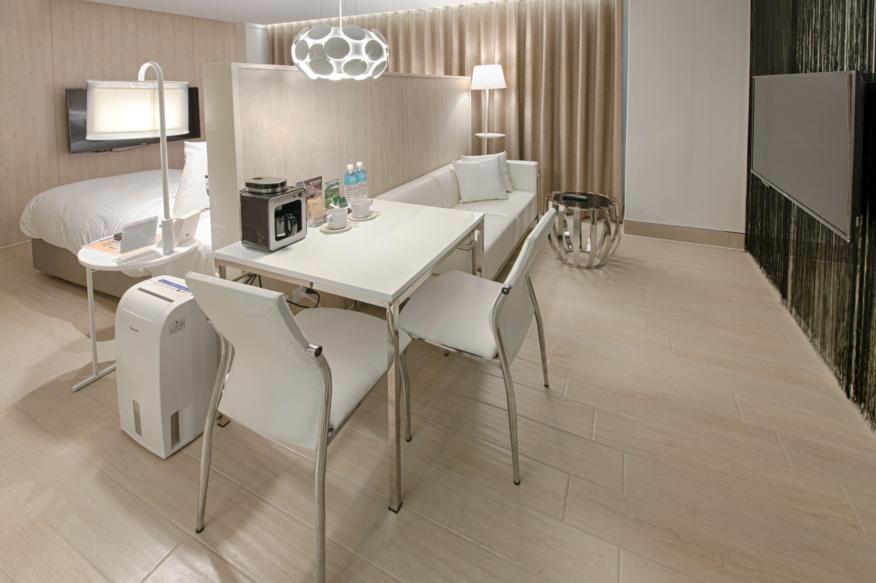 A modern hotel room with a bed, a desk with a computer, a chair, a table, and a TV.