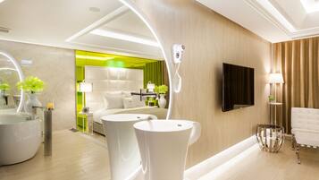 A modern hotel room with a large mirror, a round bathtub, a sofa, and a television.