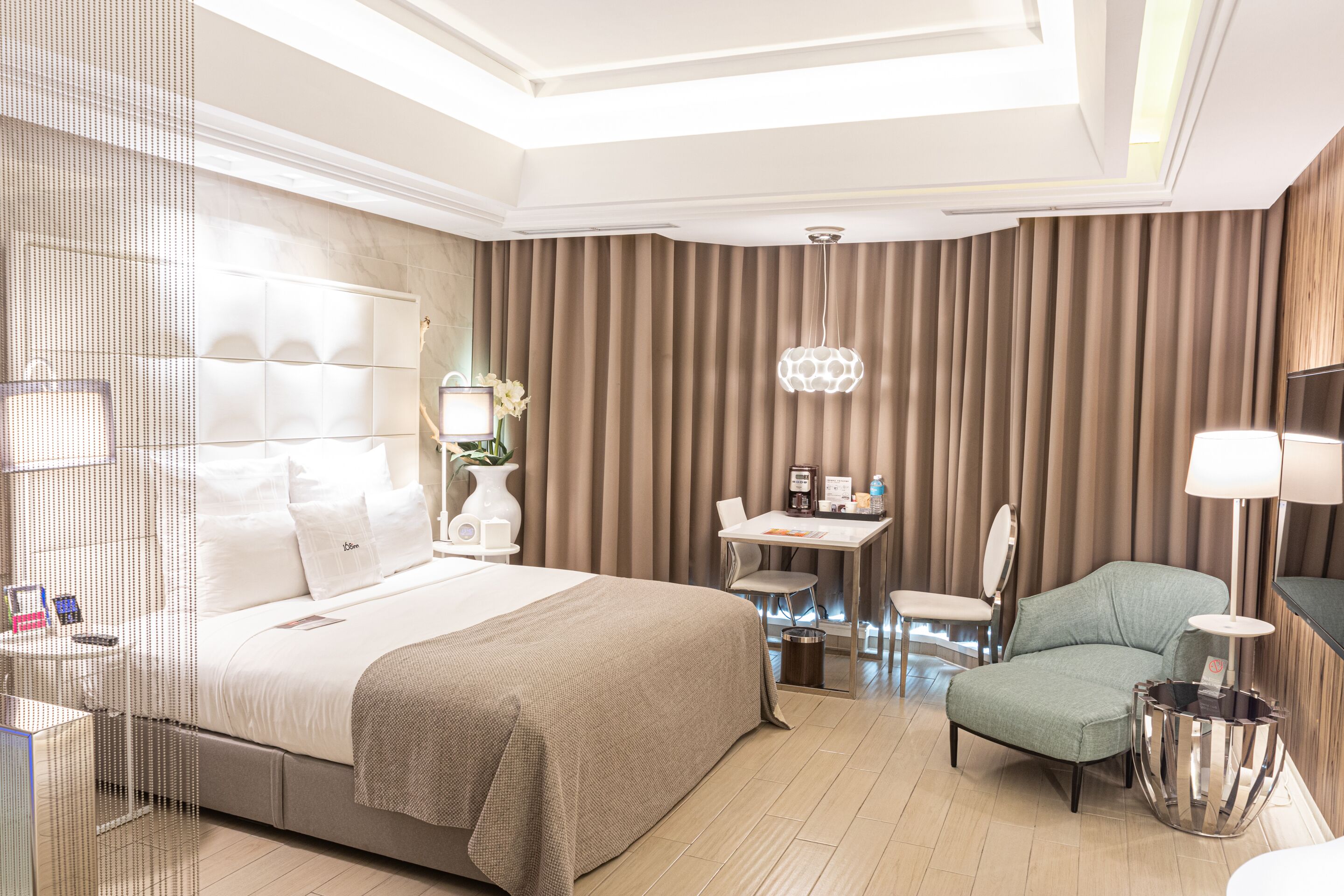 A modern hotel room with a large bed, a desk, a chair, and a small table.