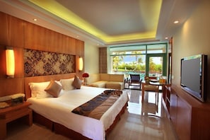 A hotel room with a large bed, a TV, a dining area with a table and chairs, and a view of the outdoors.