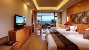 A hotel room with a TV, a laptop, a sofa, a bed, and a view of the ocean.