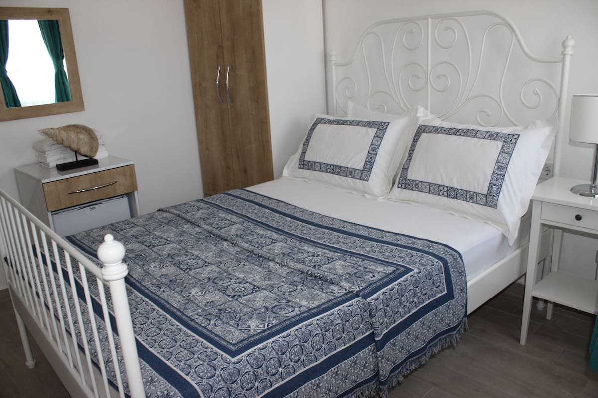 A neatly made bed with a patterned bedspread, a wooden wardrobe, and a bedside table with a lamp.