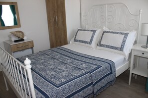 Una cama bien hecha con una colcha estampada, un armario de madera y una mesita de noche con una lámpara.