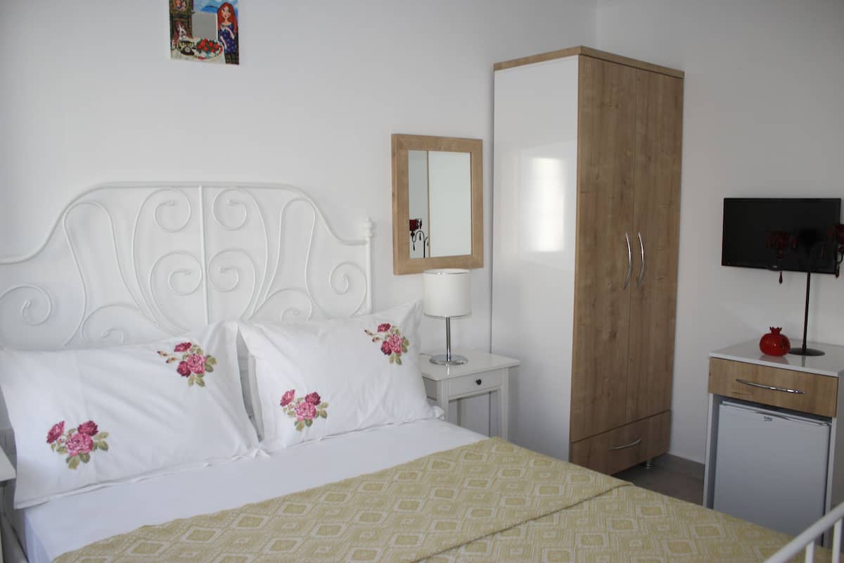 A bedroom with a bed, a nightstand, a wardrobe, a television, and a small refrigerator.