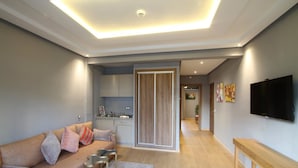A modern living room with a sofa, a coffee table, and a TV. There is a kitchen area with cabinets and a countertop. - My Loft Anfa (Casablanca)