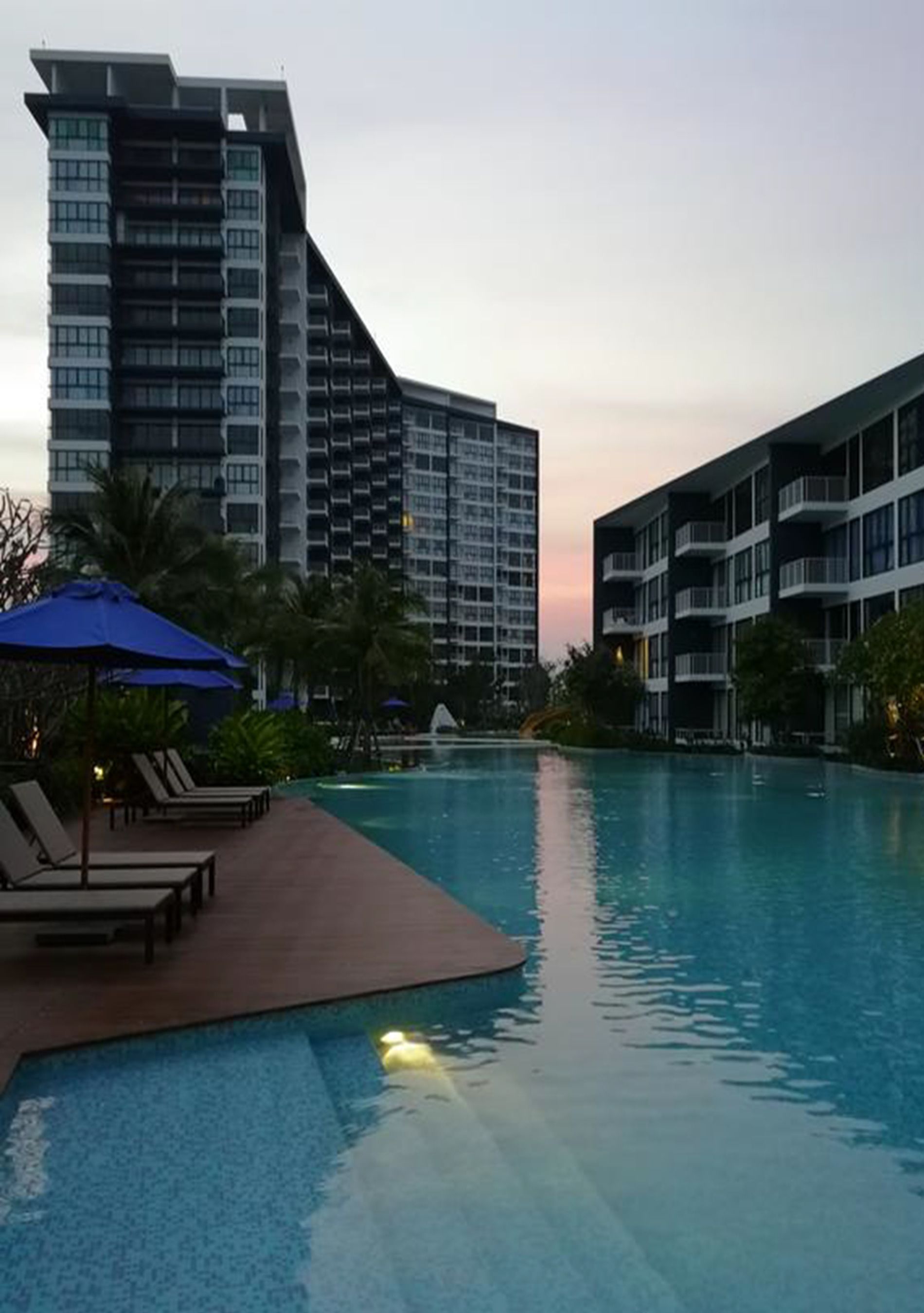 A swimming pool area with lounge chairs and umbrellas, surrounded by modern buildings.