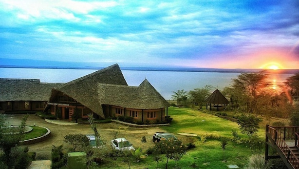 A resort with thatched-roof buildings, a pool, and a sunset view. - Sirville Lake Elementaita Lodge (Gilgil)