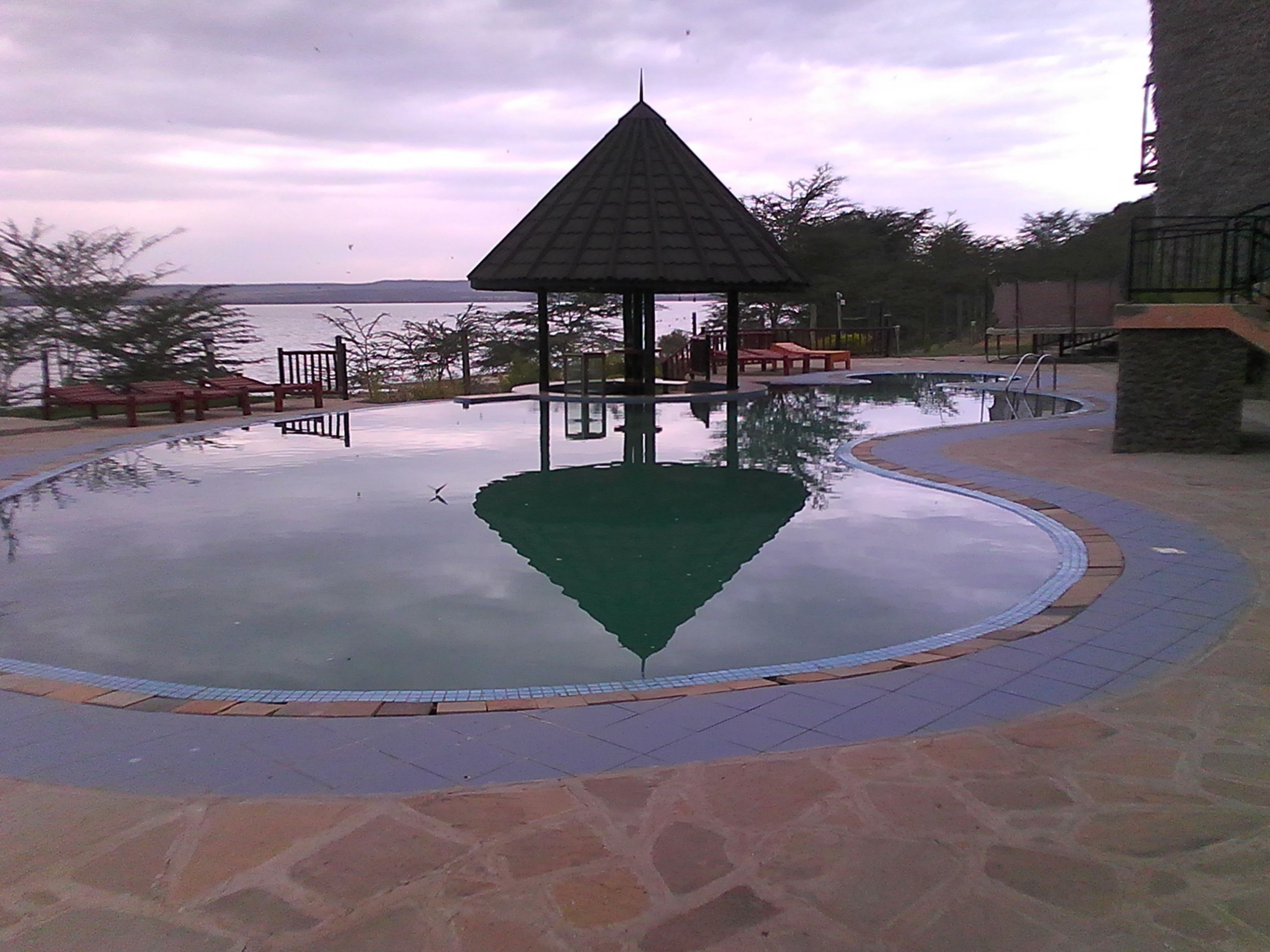 A swimming pool with a gazebo in the center, surrounded by stone tiles and benches.