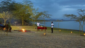 An outdoor setting with a table and chairs, a campfire, and a lake in the background. - Sirville Lake Elementaita Lodge (Gilgil)