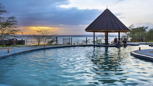 A swimming pool with a gazebo, chairs, and a view of the sunset over water. - Sirville Lake Elementaita Lodge (Gilgil)