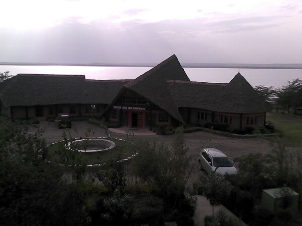 A lodge with a thatched roof, a circular driveway, and a view of a large body of water. - Sirville Lake Elementaita Lodge (Gilgil)