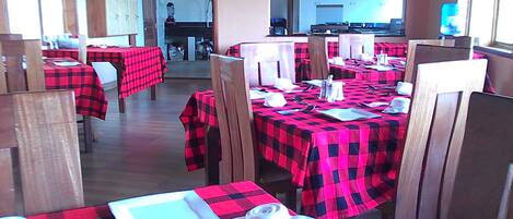Ein Restaurant mit Tischen, die mit rot-schwarz karierten Tischdecken bedeckt sind, Holzhöhlen und einer Küche im Hintergrund.