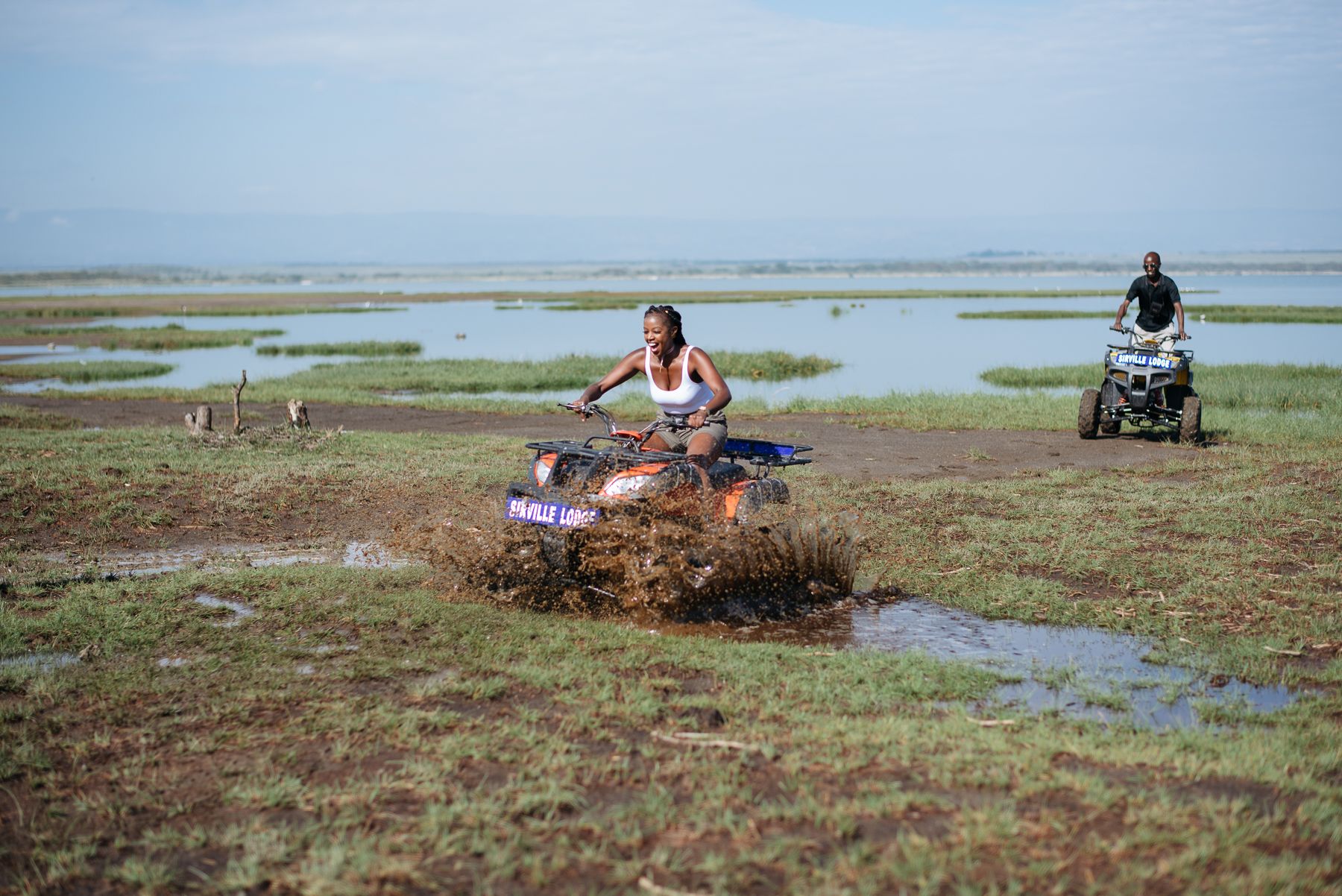 A person riding an ATV in a muddy field with water puddles.