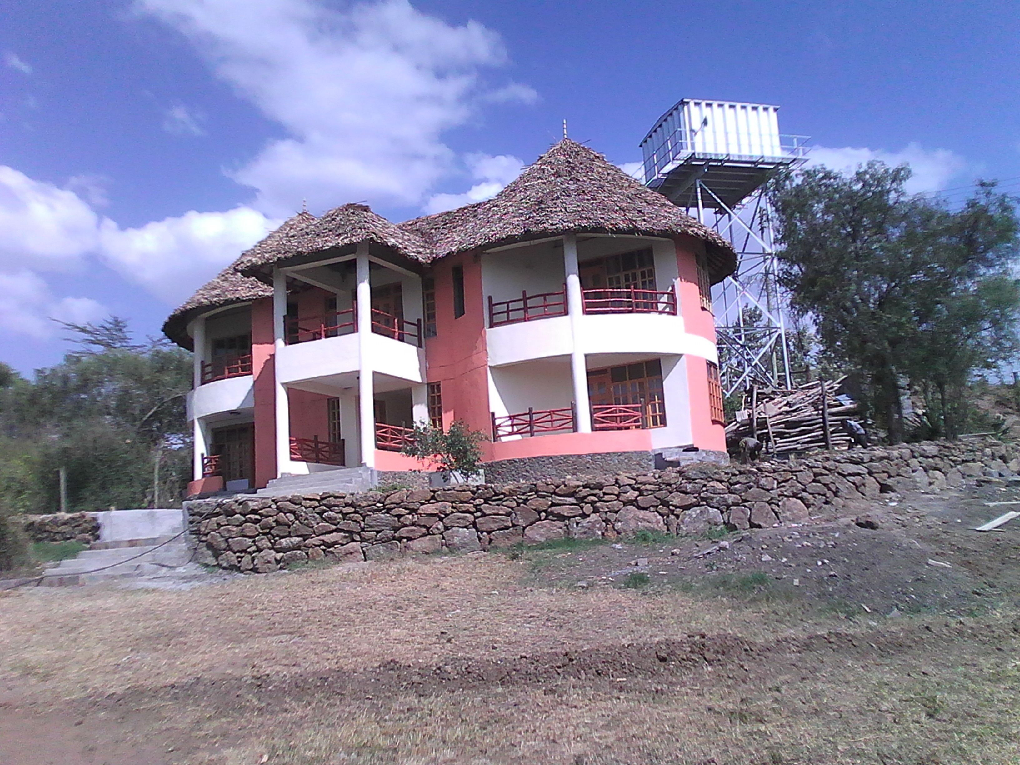 Un bâtiment à deux étages, à l’extérieur rouge et blanc, avec un toit de chaume et un château d’eau situé à proximité.