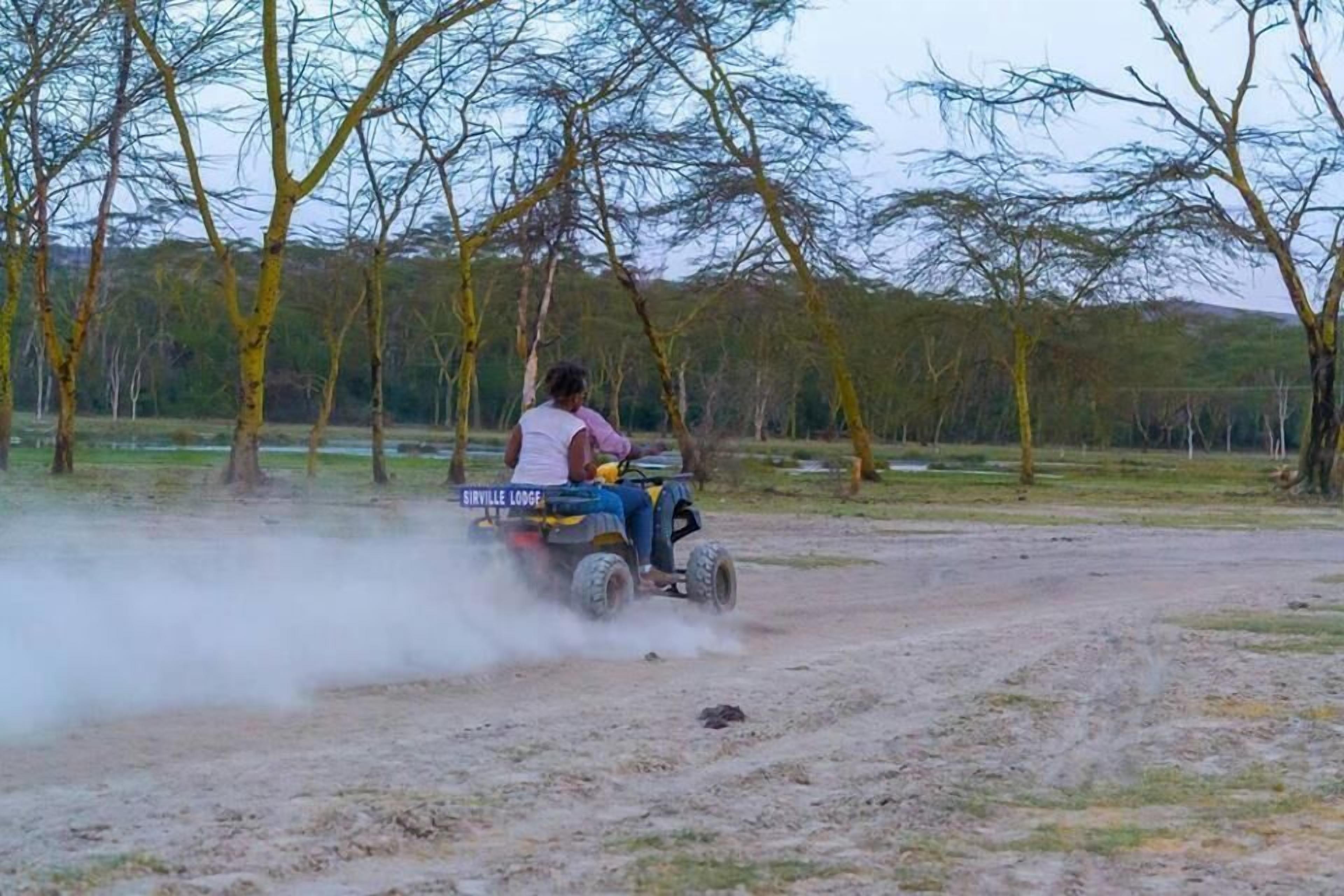 A person driving a quad bike on a dirt path with trees in the background.