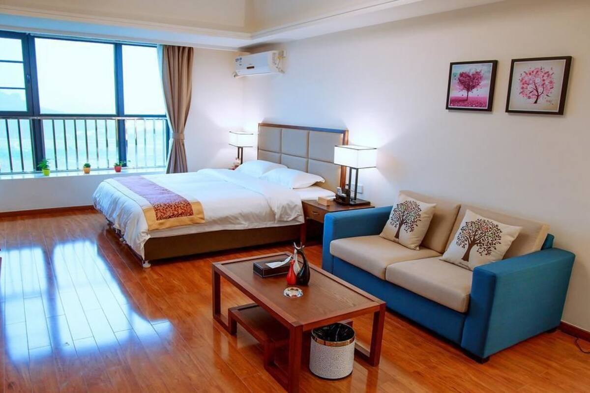 A hotel room with a bed, a blue sofa, a wooden coffee table, and a window with curtains.