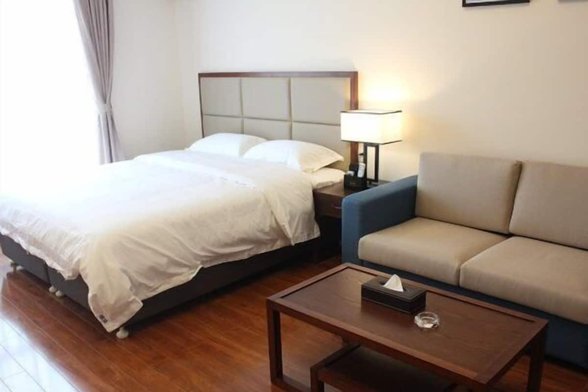 A hotel room with a bed, a sofa, a nightstand with a lamp, and a wooden coffee table.