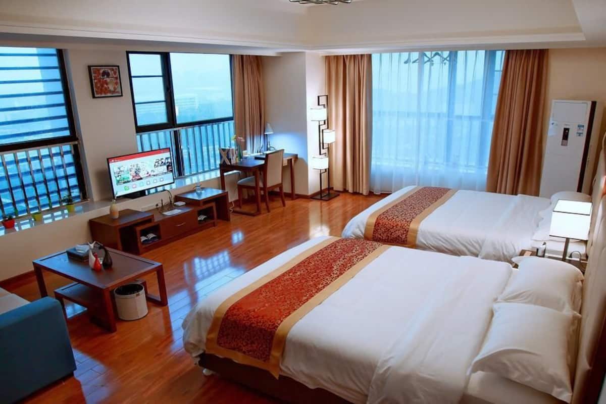 A hotel room with two beds, a desk, a chair, and a TV.