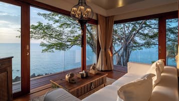 A room with a large window overlooking a body of water, a wooden floor, a white sofa, a wooden coffee table, and a decorative lamp.