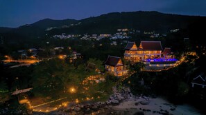 A large, multi-story building with a traditional architectural style, surrounded by a landscaped garden and a view of a hillside. - Villa Riva (Koh Samui)