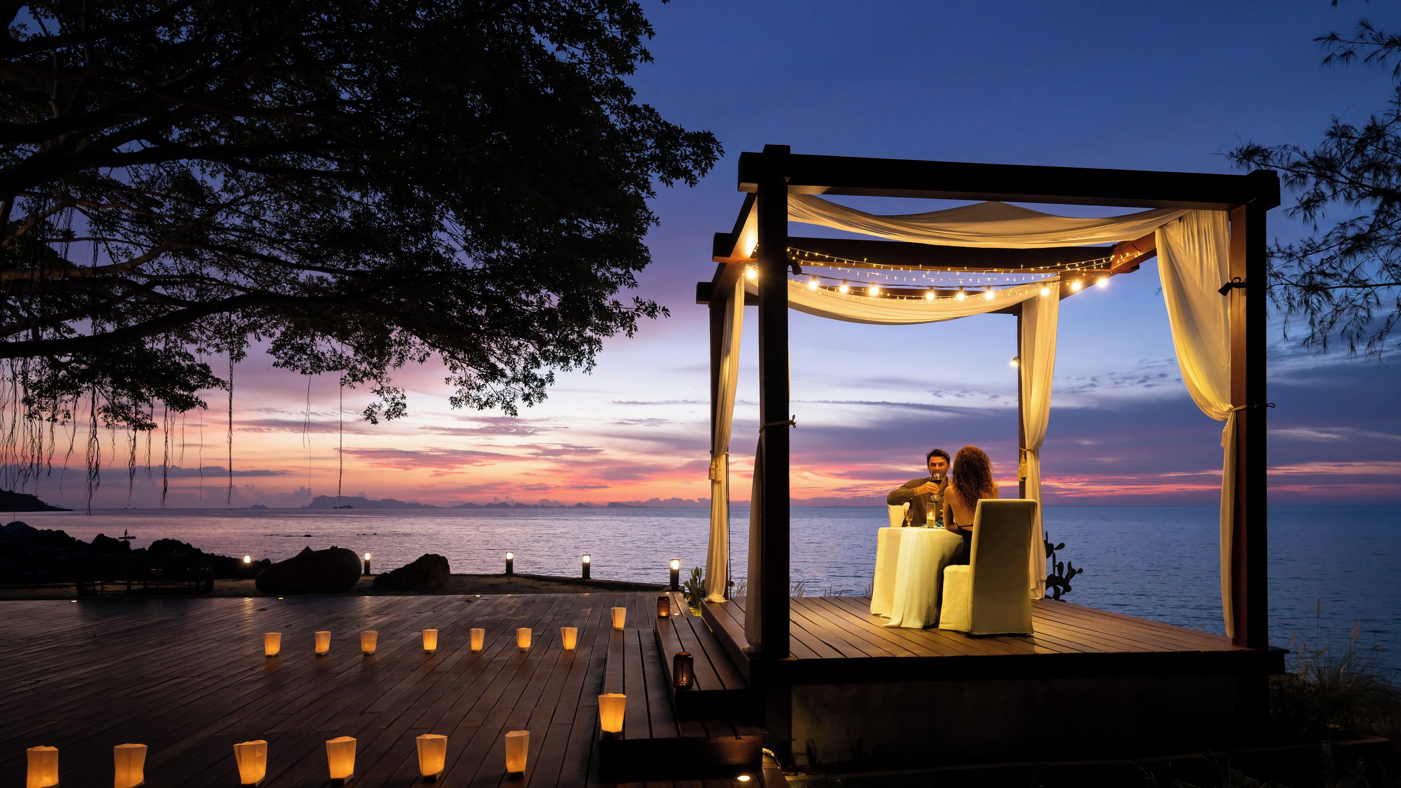 A wooden deck with a canopy and candles, overlooking a body of water.